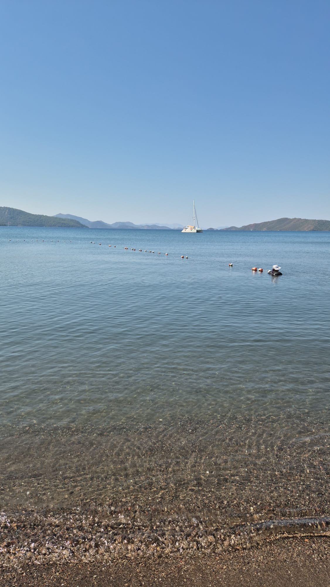 Clear shallow water, a sailboat and distant hills in Hisaronu Bay